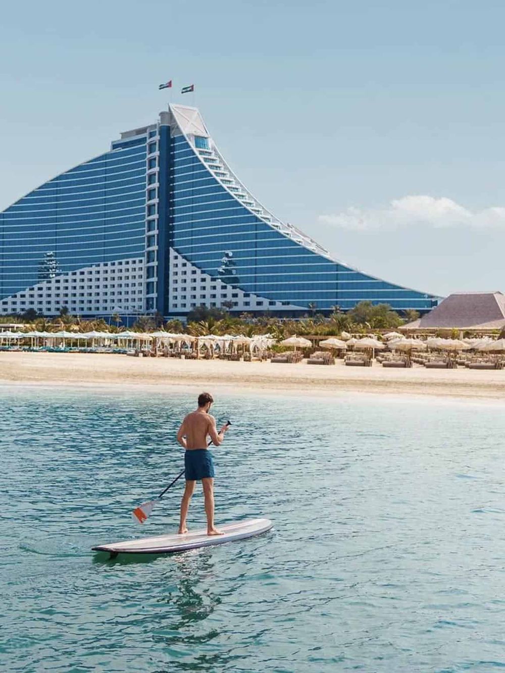 Modern luxury hotel on sandy beach with paddleboarding activities nearby.