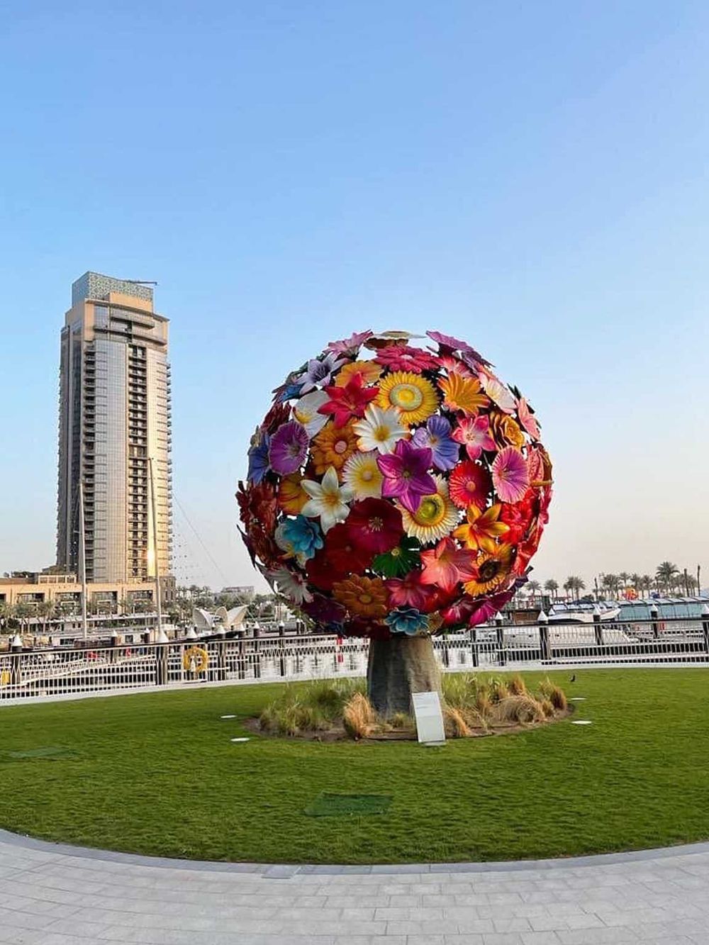 Colorful floral globe sculpture at Quest for Directions marina waterfront, showcasing artistic landscaping and modern city views.