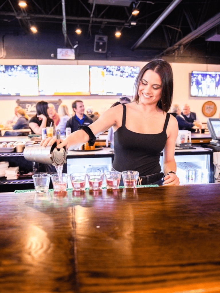 Refreshing bartender pouring colorful drinks at a lively bar scene.