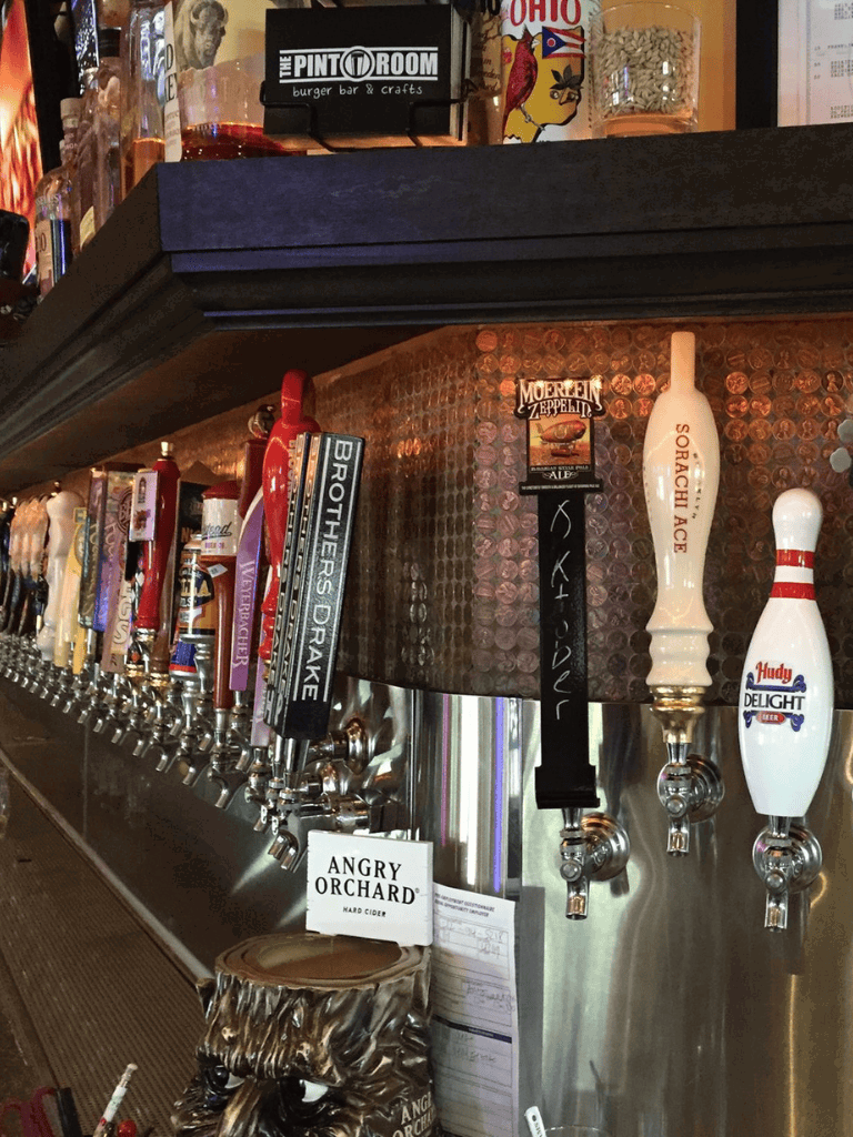 A row of beer taps at a bar with various craft beer brands and cider options.