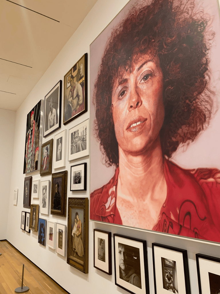 Vivid portrait of a woman with curly hair displayed in an art gallery wall of assorted artworks and photographs.