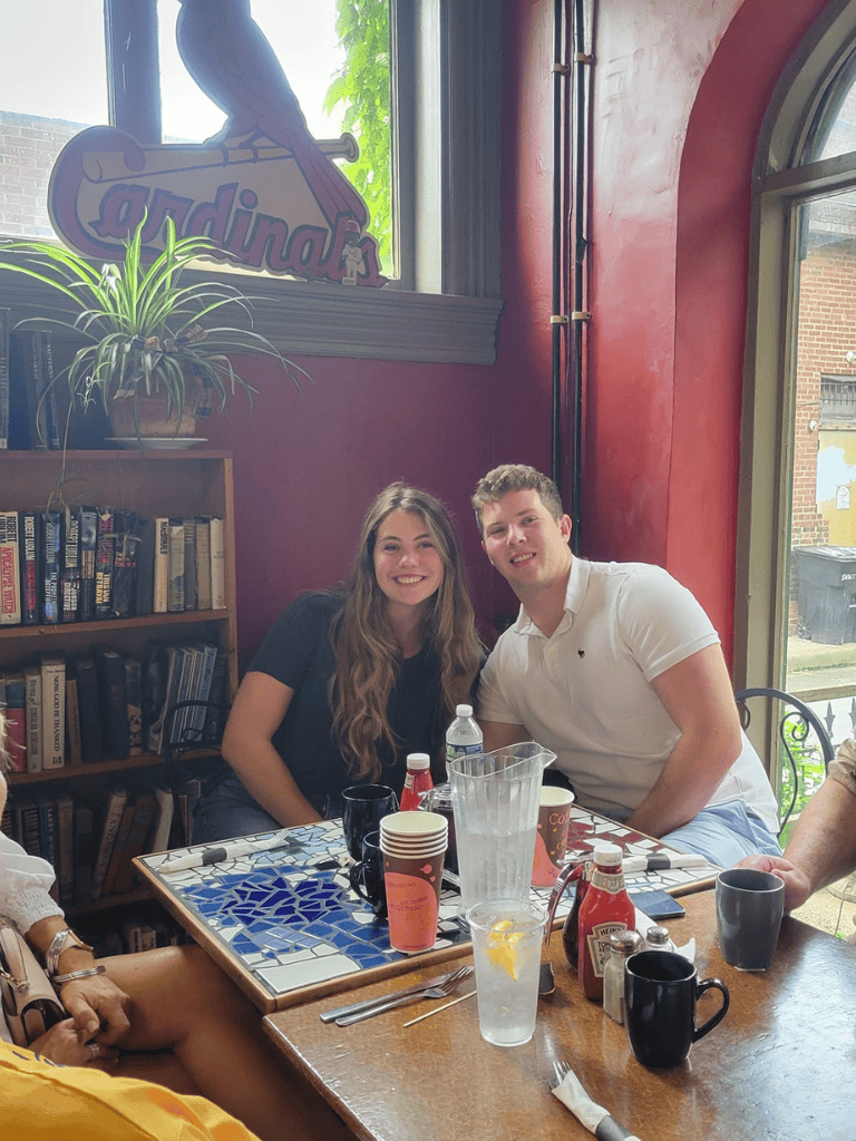 Young adults enjoying a meal at a cozy restaurant with bookshelf decor and natural light.