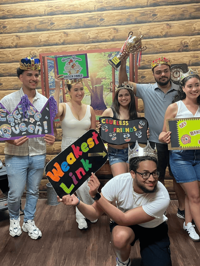 Happy team celebrating at QuestForDirections, wearing crowns, holding colorful signs, and winning a chicken dinner.