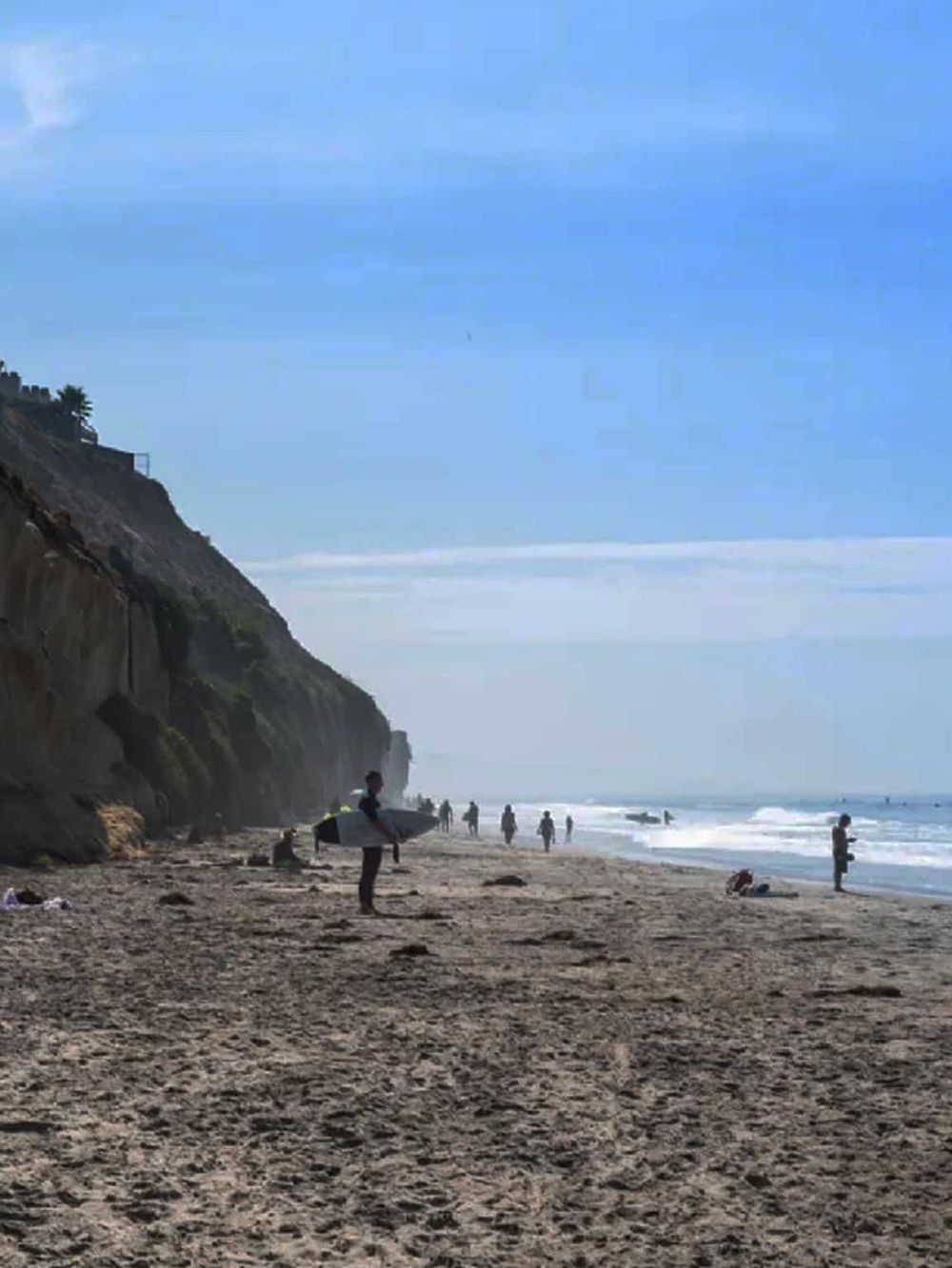 Surfing at the beach with people enjoying the sunny coastal scenery and ocean waves, ideal for surfing and beach activities.