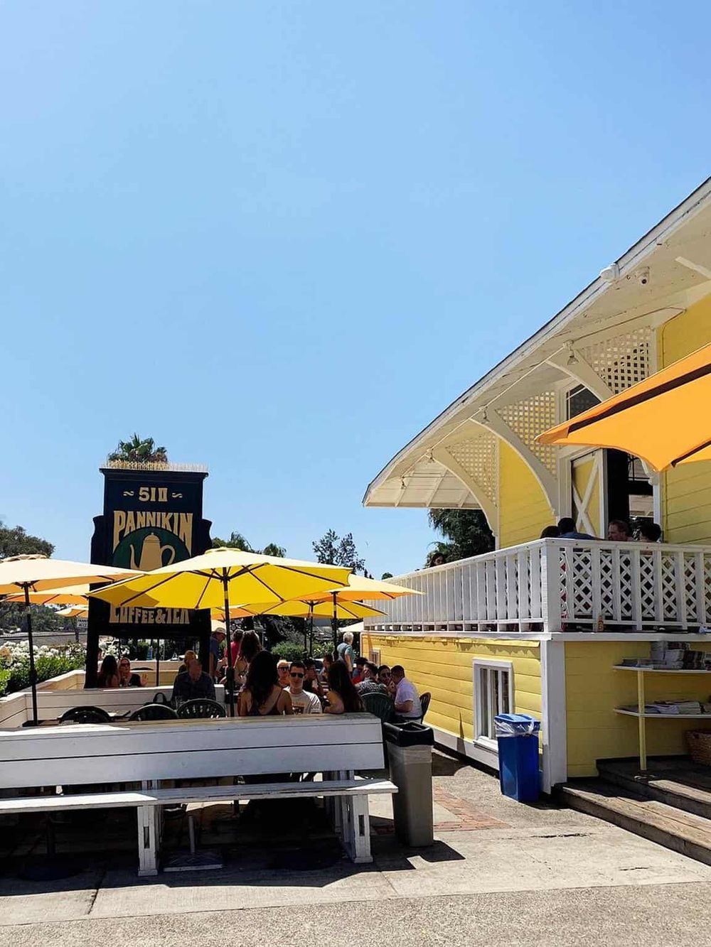 Outdoor dining at a sunny neighborhood restaurant with yellow umbrellas and a lively atmosphere.
