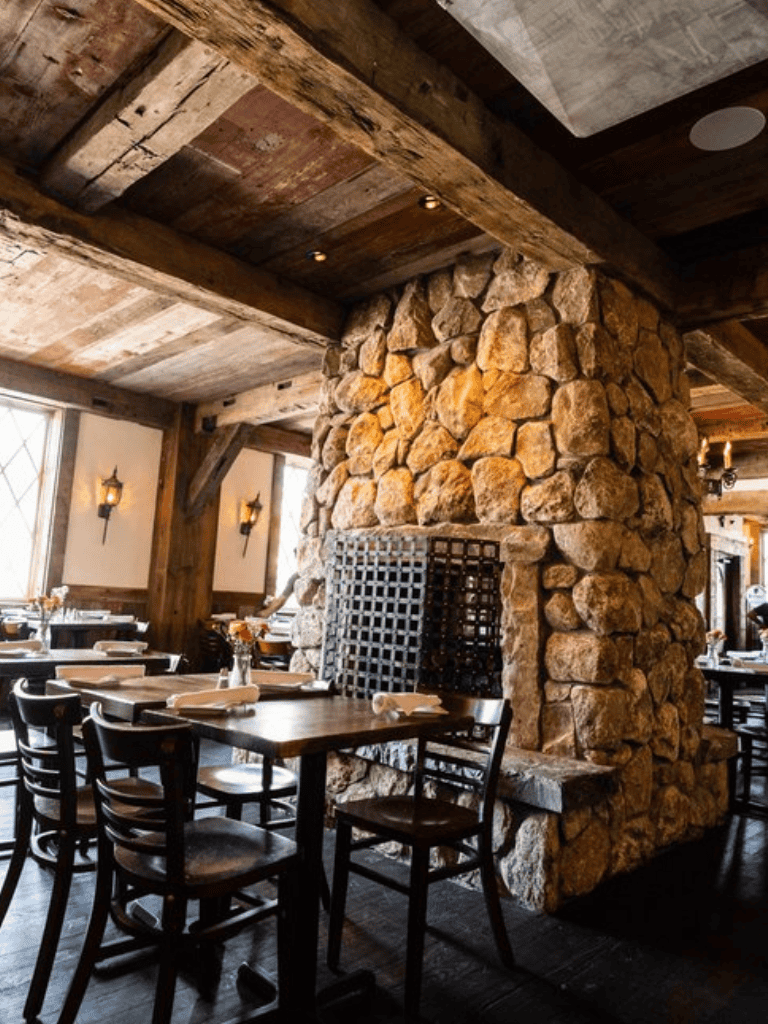 Warm rustic restaurant interior with stone fireplace and wooden beams, perfect for cozy dining.