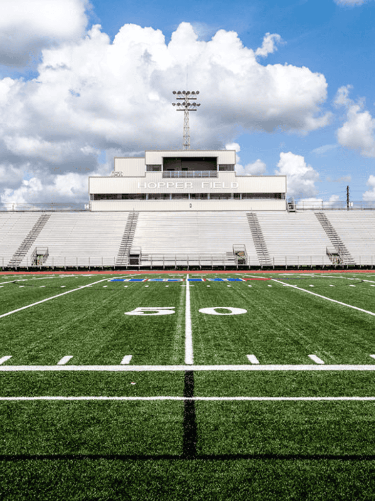 Bright green football field at Hopper Field with stadium bleachers and sky.