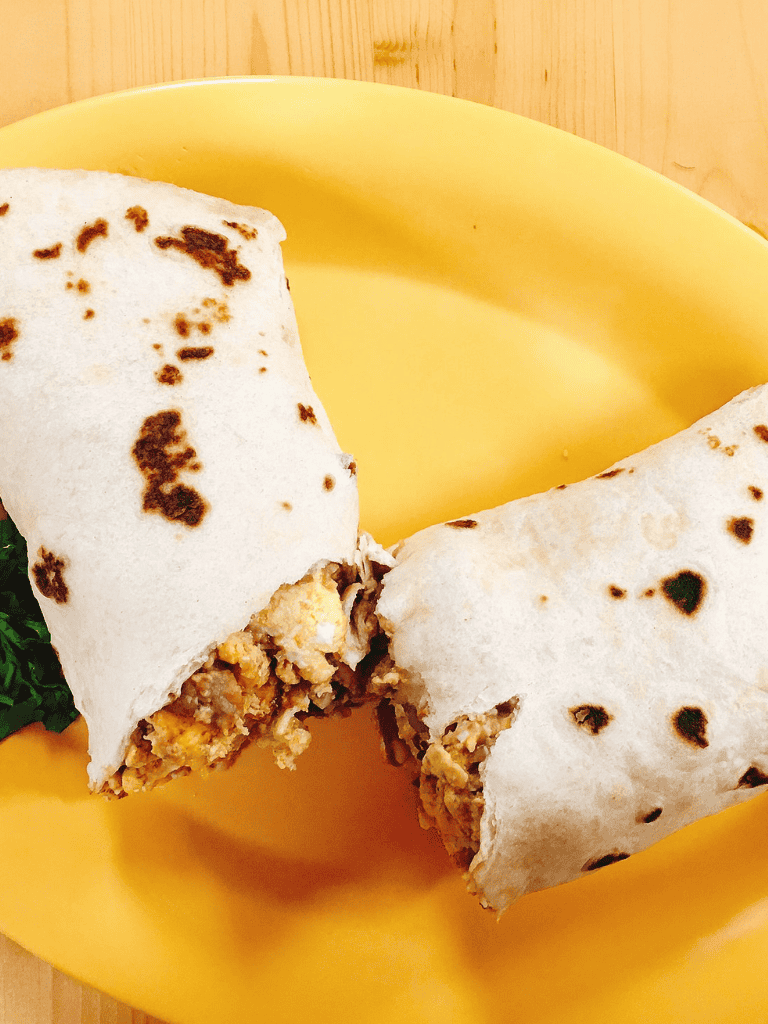Soft taco wrap with spiced meat filling on yellow plate, wooden background.
