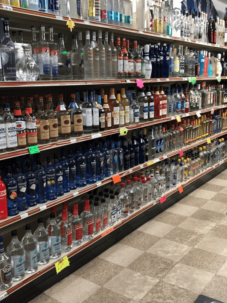 Bottles of various alcoholic beverages on store shelves in a liquor aisle.