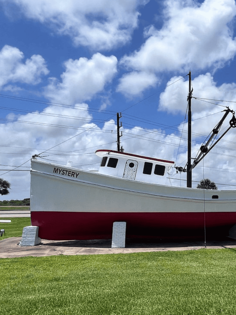 Boat with the name "Mystery" on display outdoors under a blue sky with fluffy clouds.
