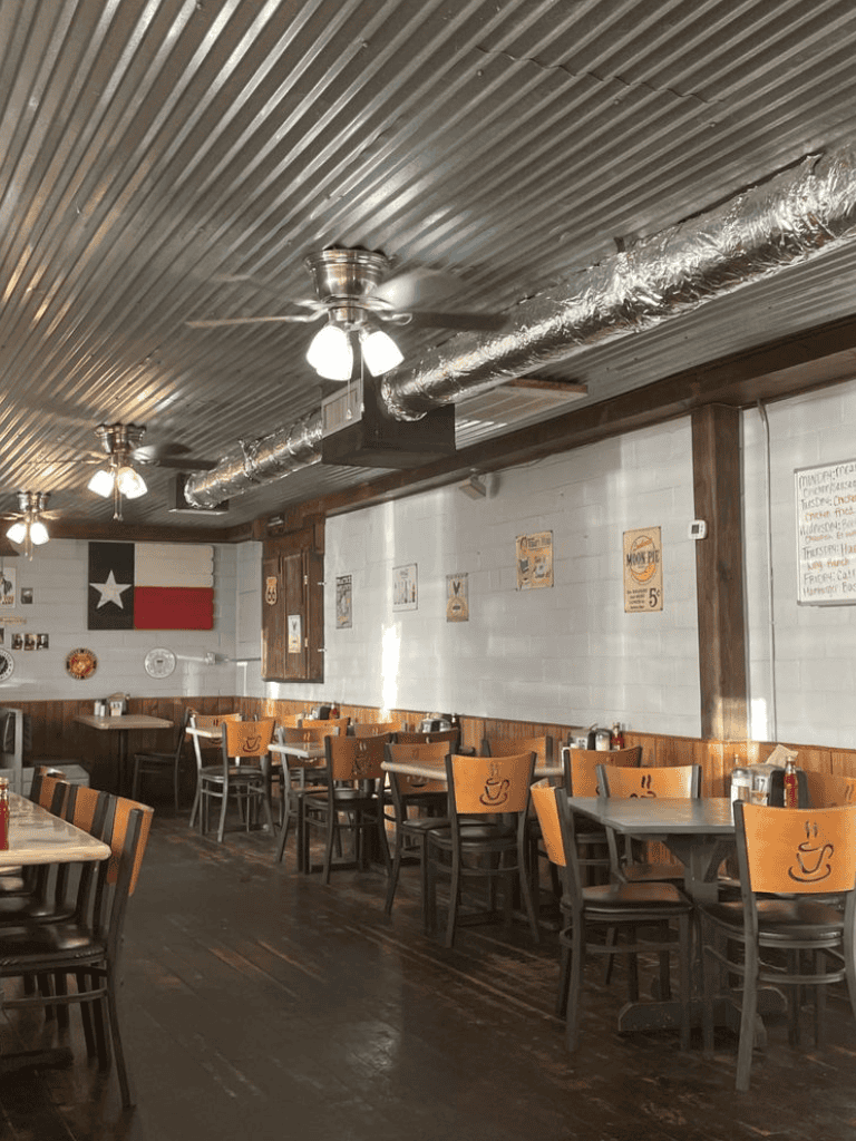 Warm interior of a cozy cafe with wooden tables and chairs, Texas flag decor, and ceiling fans.