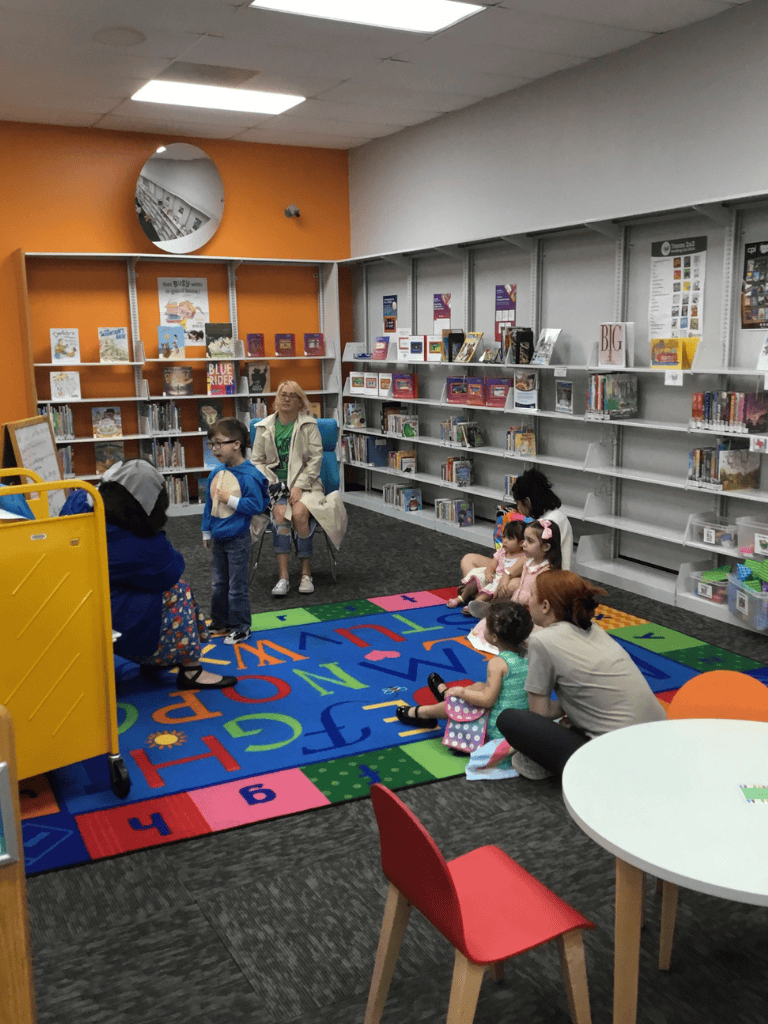 1. Children’s storytime in a colorful library reading corner with bookshelves.