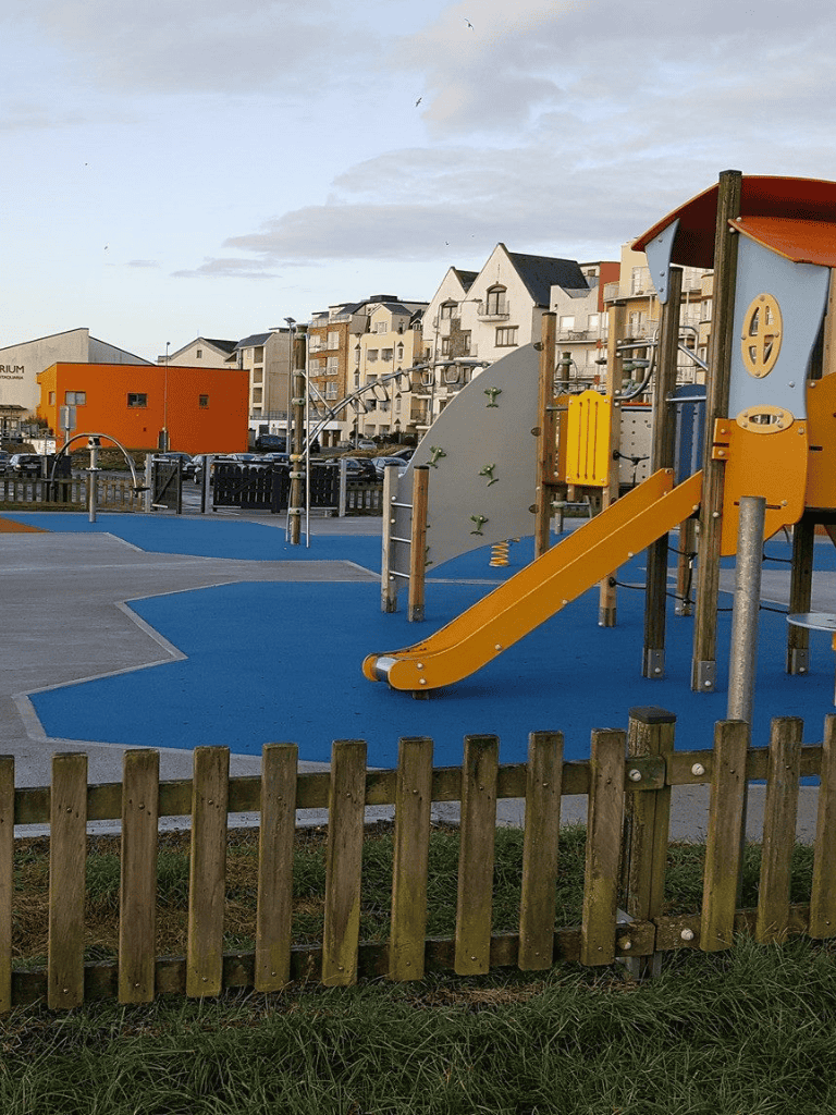 Colorful children's playground with slide and climbing features in a residential area with modern buildings.