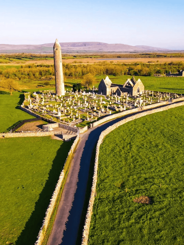 Ancient Irish round tower and historic site with cemetery, scenic rural landscape, and rolling hills in Ireland.