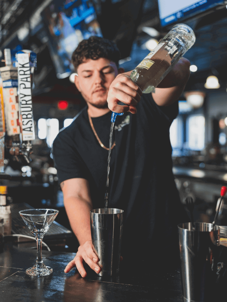 Young bartender pouring liquor into shaker at bar.