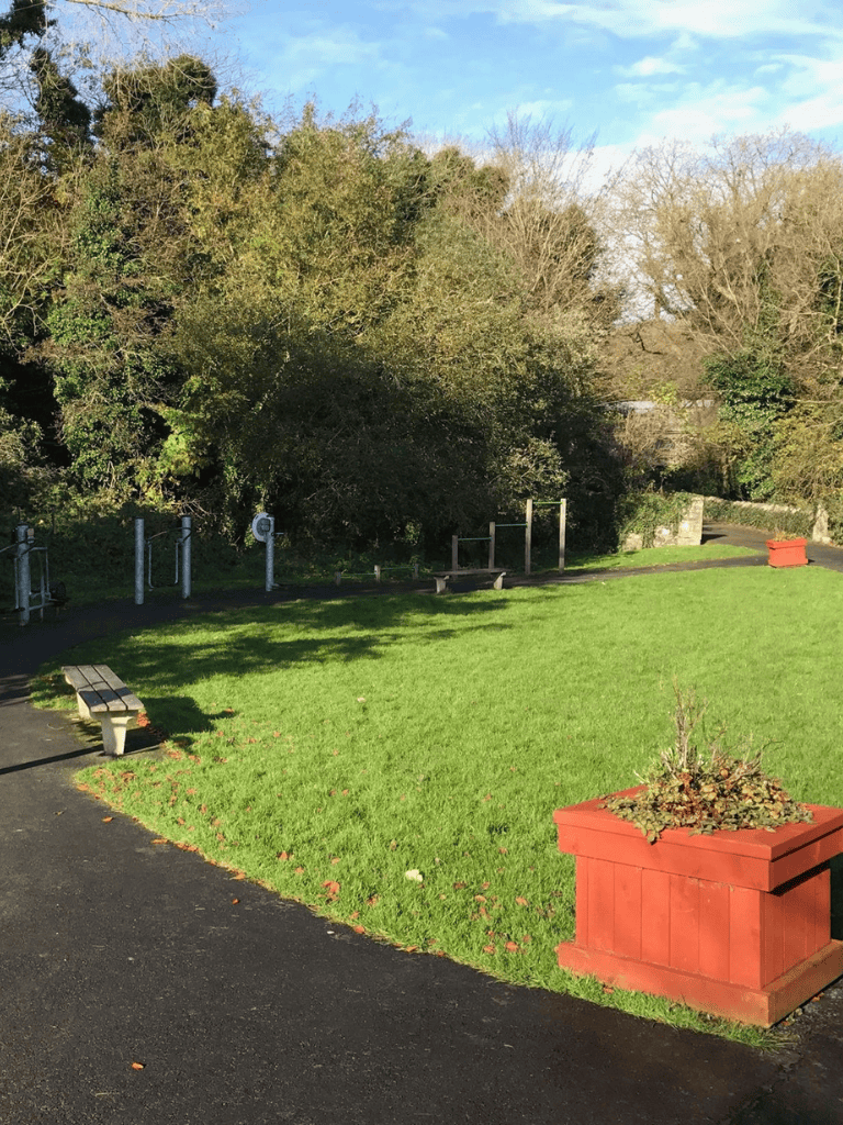 Open outdoor park with benches, lush green grass, and mature trees; ideal for relaxation and nature walks.