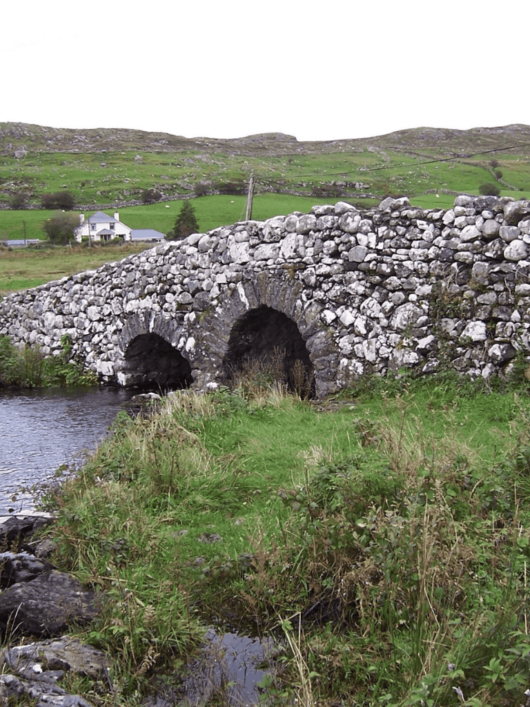 Ancient stone bridge over a river in lush green countryside, scenic rural landscape, Ireland.