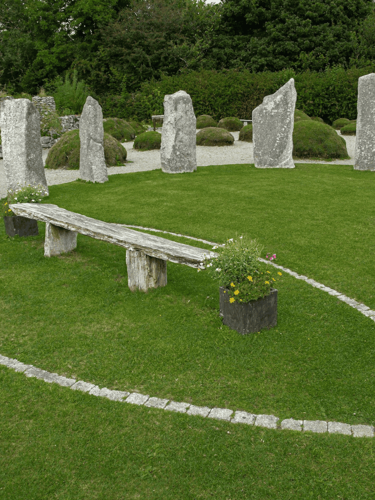 Ancient stone circle with grass and wooden bench, lush greenery background, peaceful garden setting.