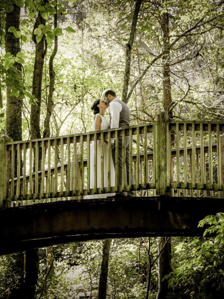A couple kissing on a wooded bridge during daytime in a lush green forest.