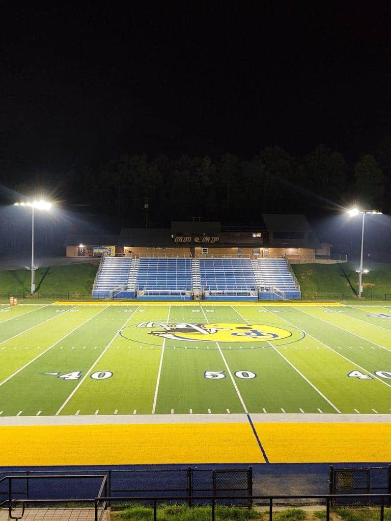 Brightly lit football field at night with stadium seating and goalposts.
