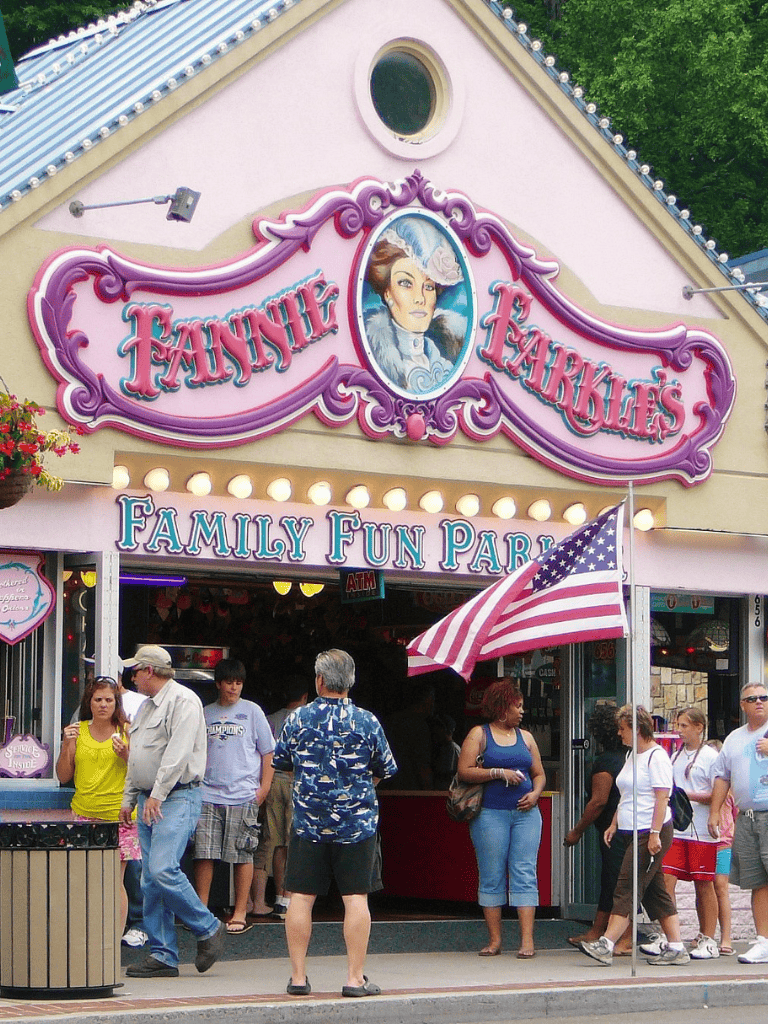 Colorful Fannie Fayke's Family Fun Park entrance with visitors and American flag in front.