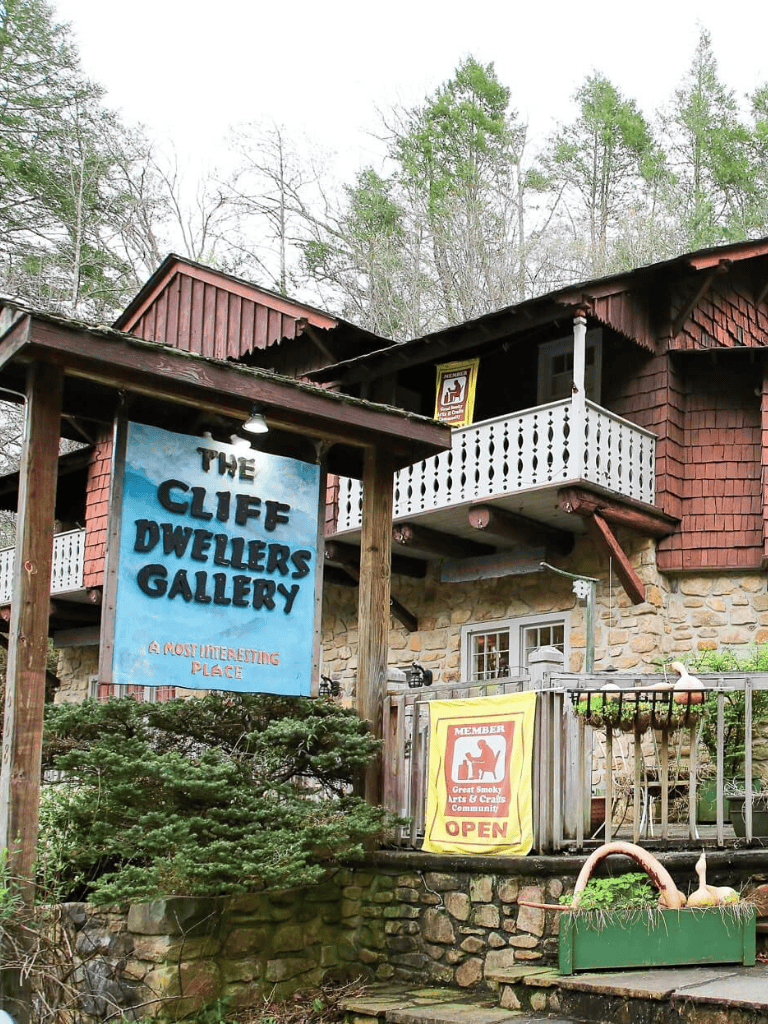Colorful Cliff Dwellers Gallery sign, rustic building, and outdoor seating in a scenic mountain setting.