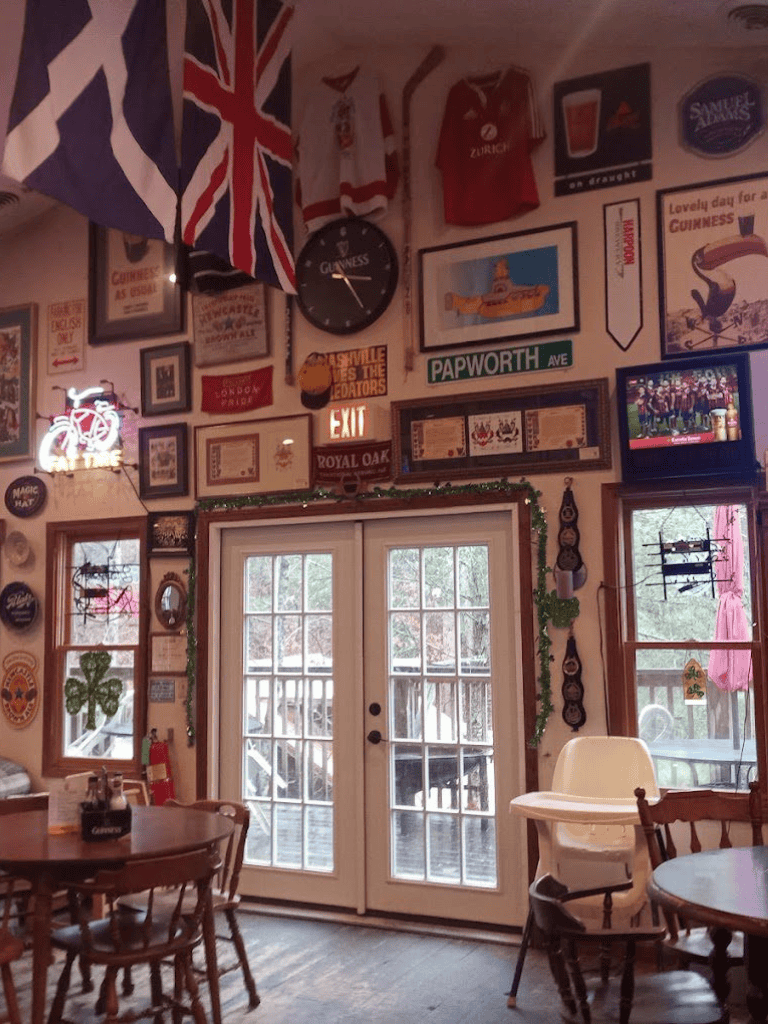 Cozy pub interior decorated with flags, vintage signs, and a large wall clock, creating a welcoming atmosphere.