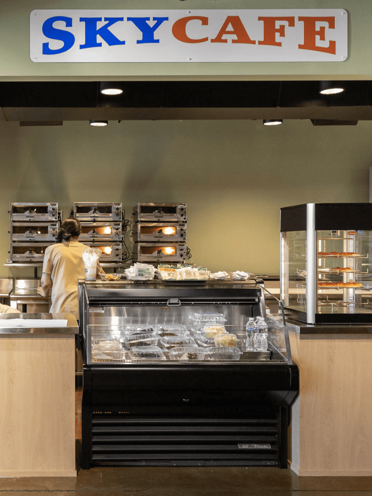 Quick-service pizza shop with heated ovens, food display case, and a worker preparing meals.