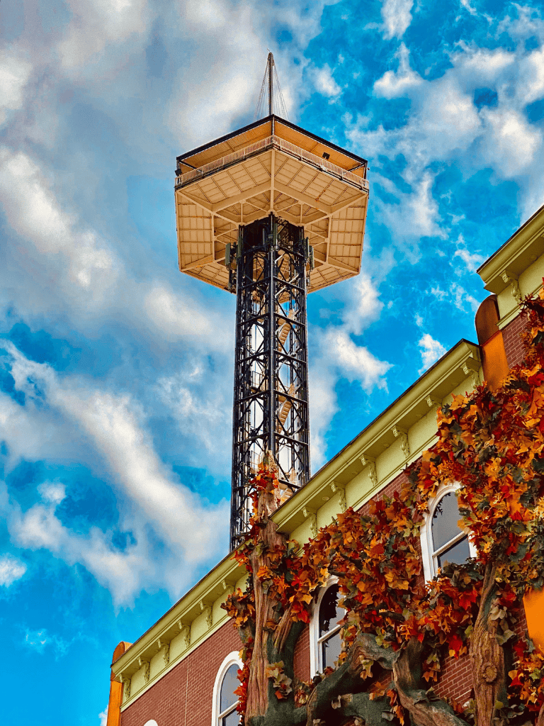 Colorful historic fire tower with autumn foliage, cityscape, bright sky, QuestForDirections navigation aid.