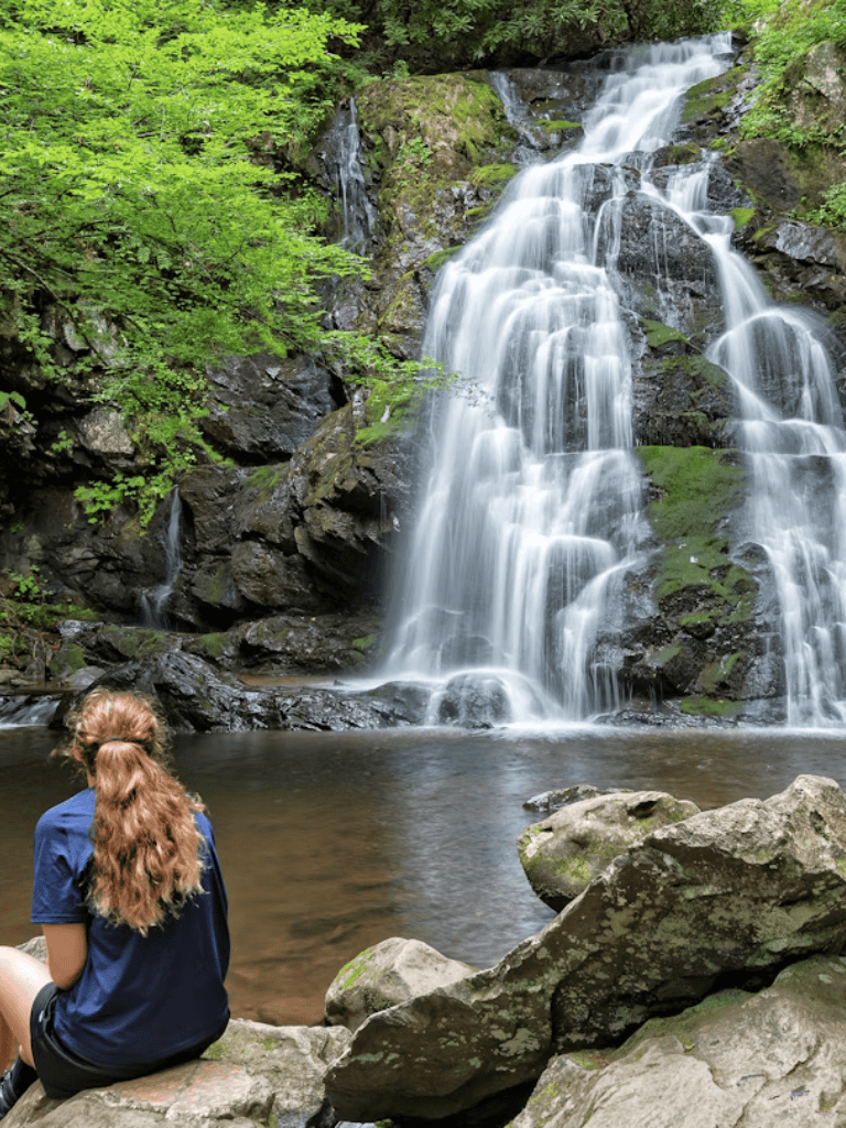 Waterfall in lush green forest with person sitting on rocks, scenic nature trail at QuestForDirections.
