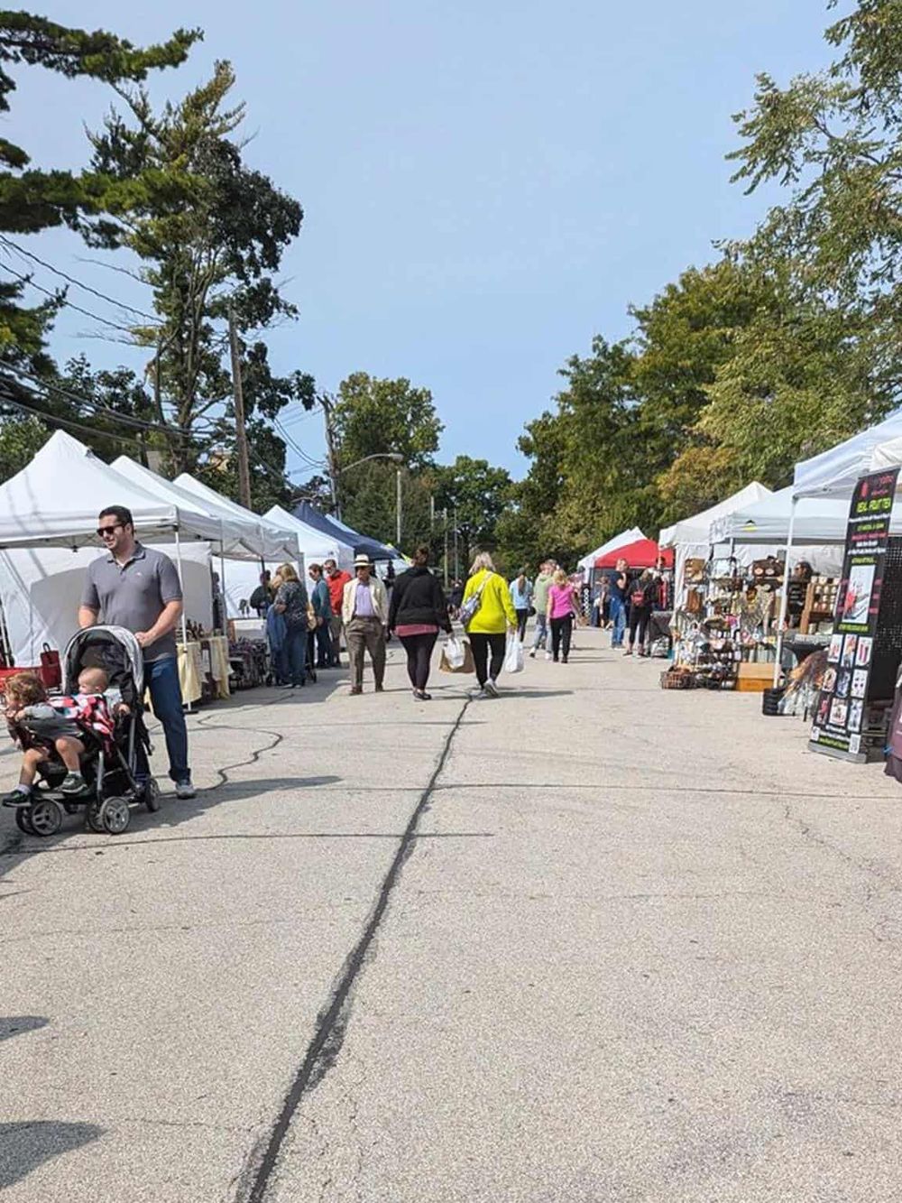 Colorful outdoor market with white tents, shoppers, and vendor stalls on a bright day.