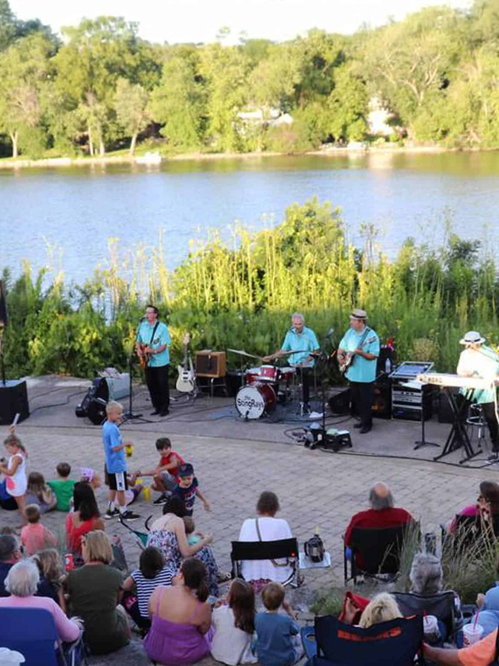 Outdoor live music performance at sunset near a lake, family-friendly event with audience enjoying local entertainment.