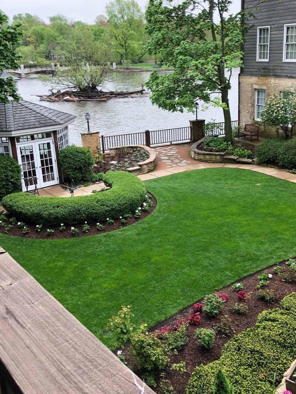 Lush backyard garden with well-maintained lawn, decorative shrubs, and a view of the river and island.