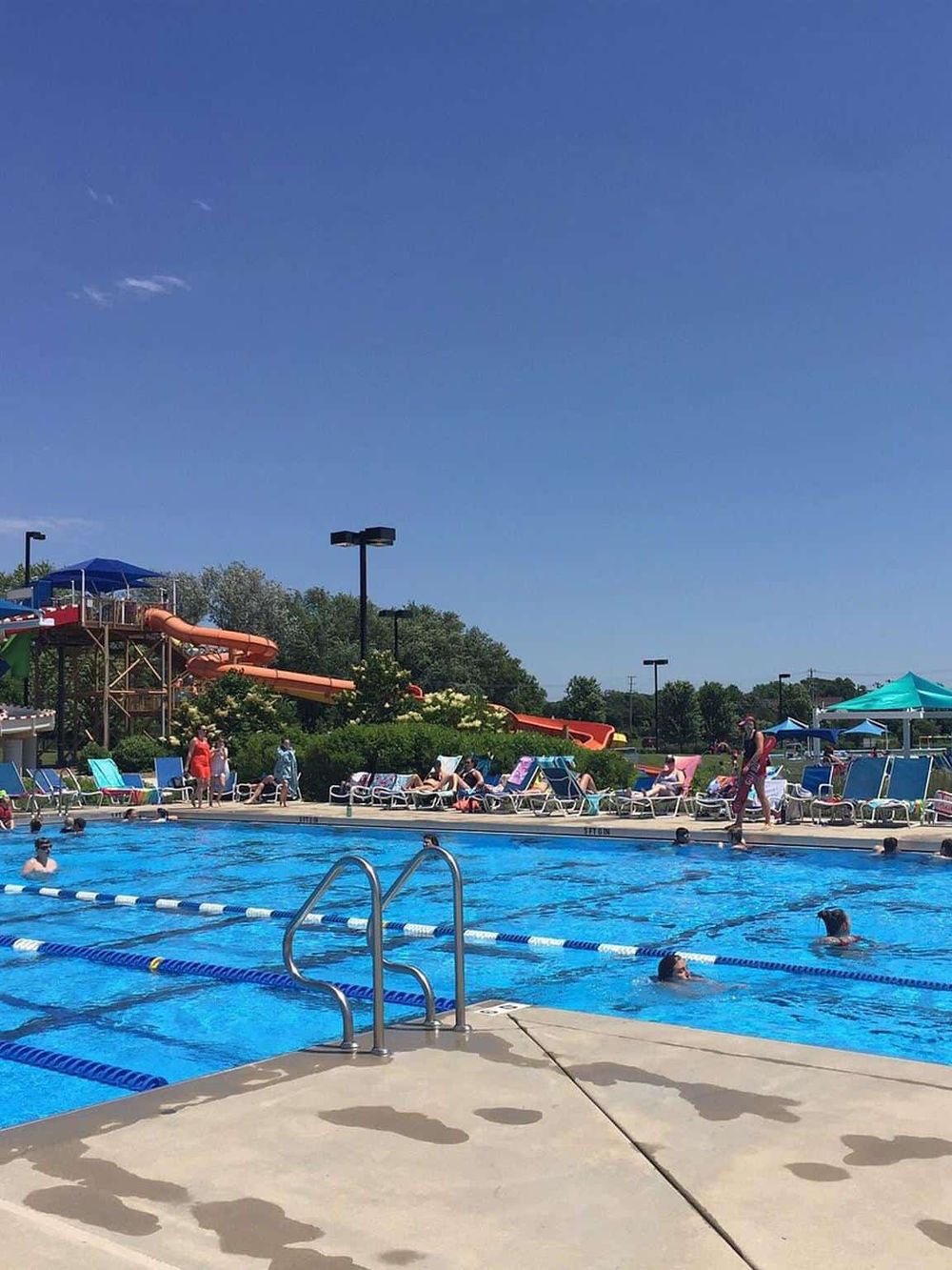 Children's water park with slides, swimming pool, sunbathers, and family fun on a sunny day.