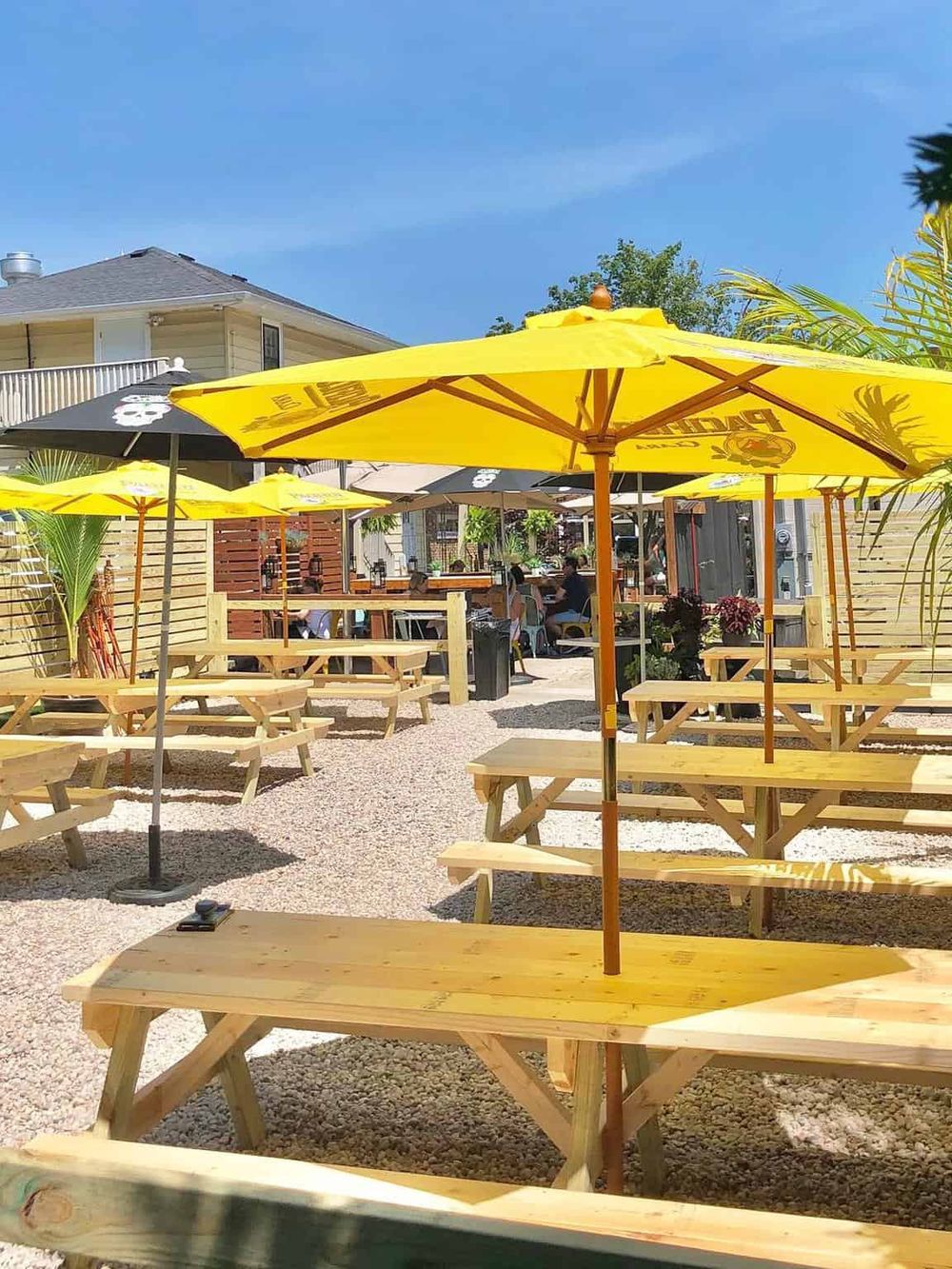 Outdoor restaurant patio with yellow umbrellas and wooden picnic tables under sunny skies.