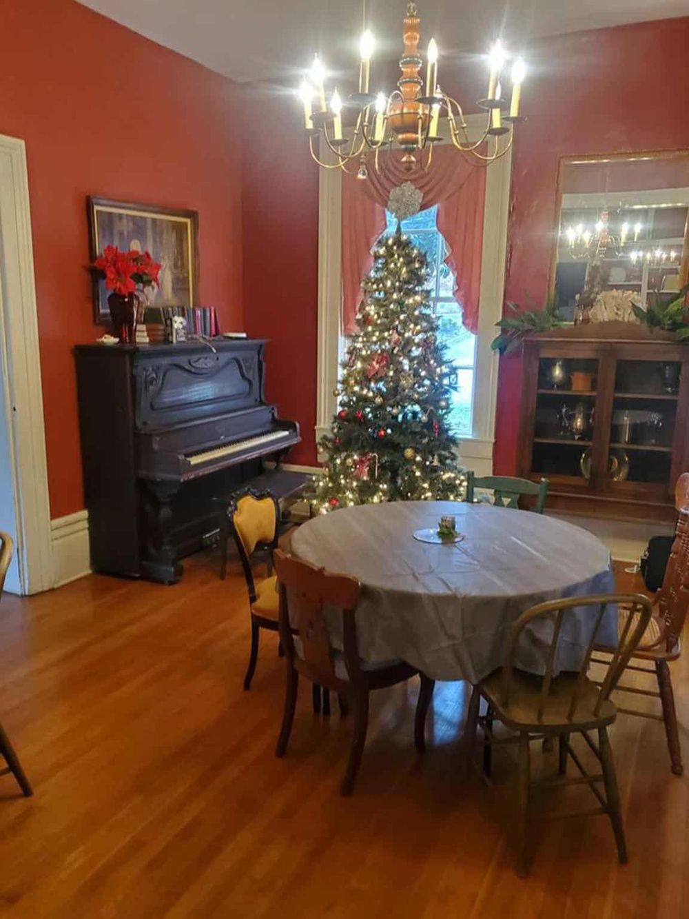 Festive dining room with decorated Christmas tree, vintage furniture, and elegant chandelier, ideal for holiday celebrations.
