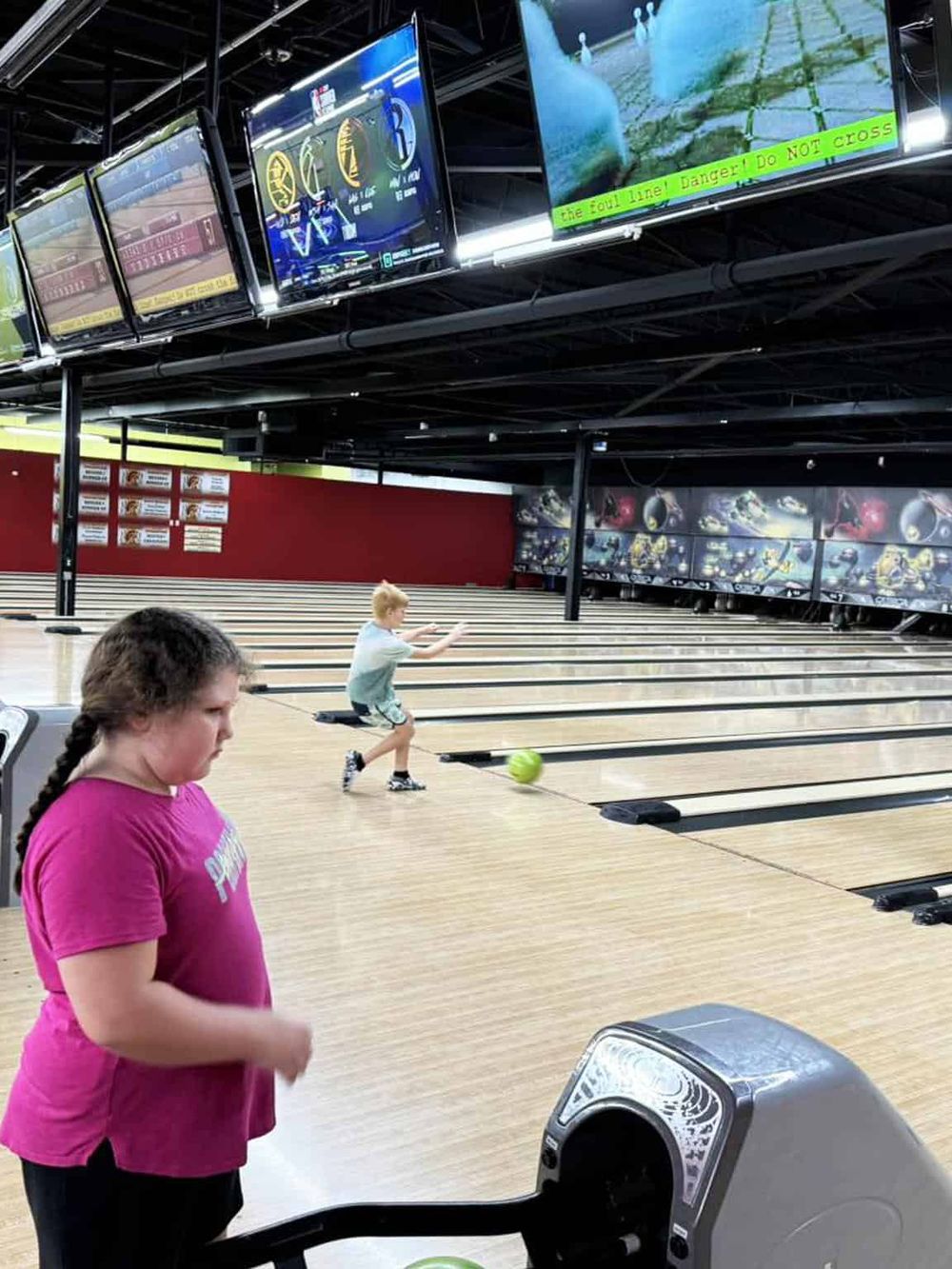Kids bowling alley with digital screens and warning sign on foul line, family fun activity at QuestForDirections.