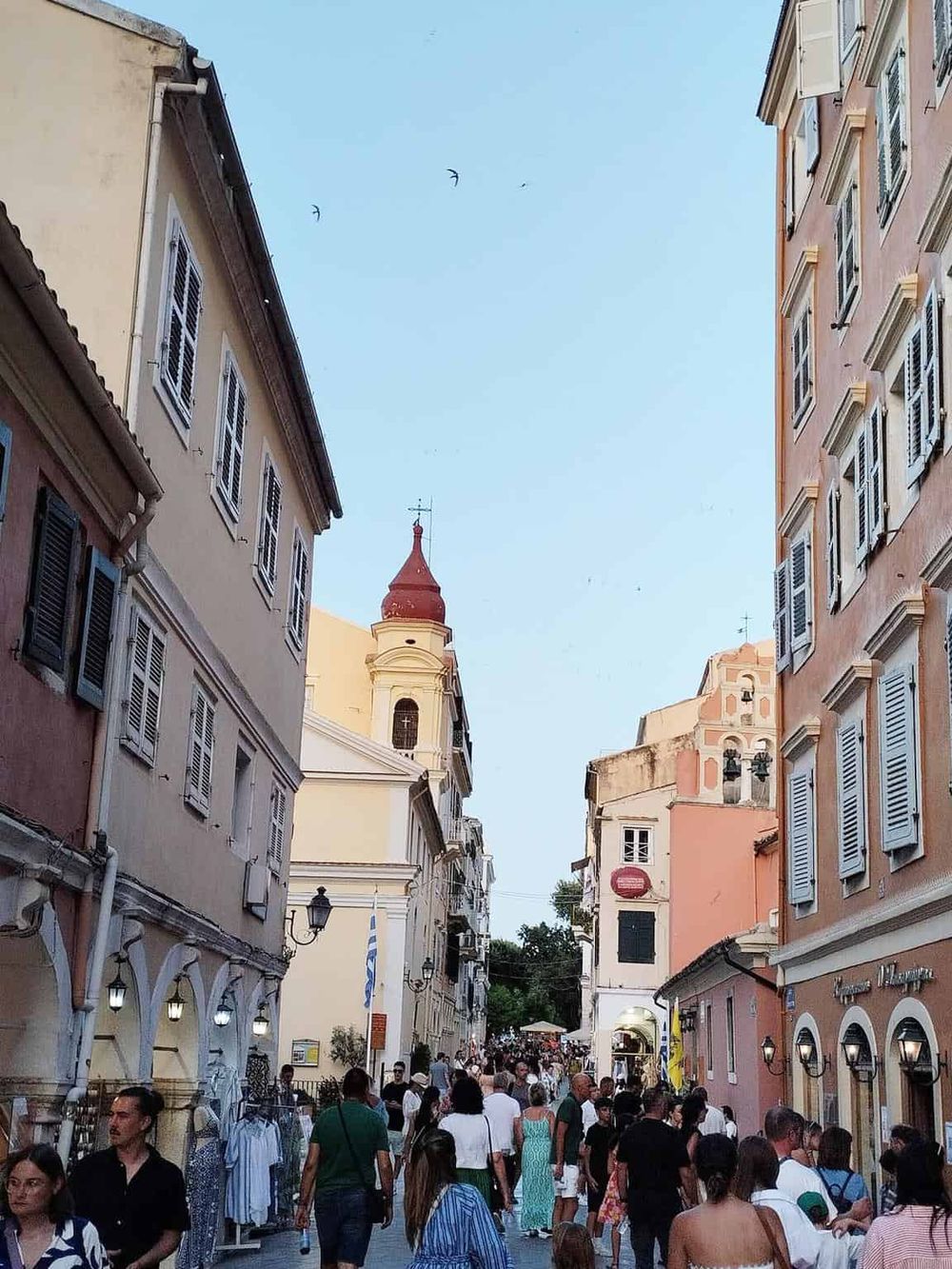 Bustling Greek street scene with historic architecture and people shopping and exploring.