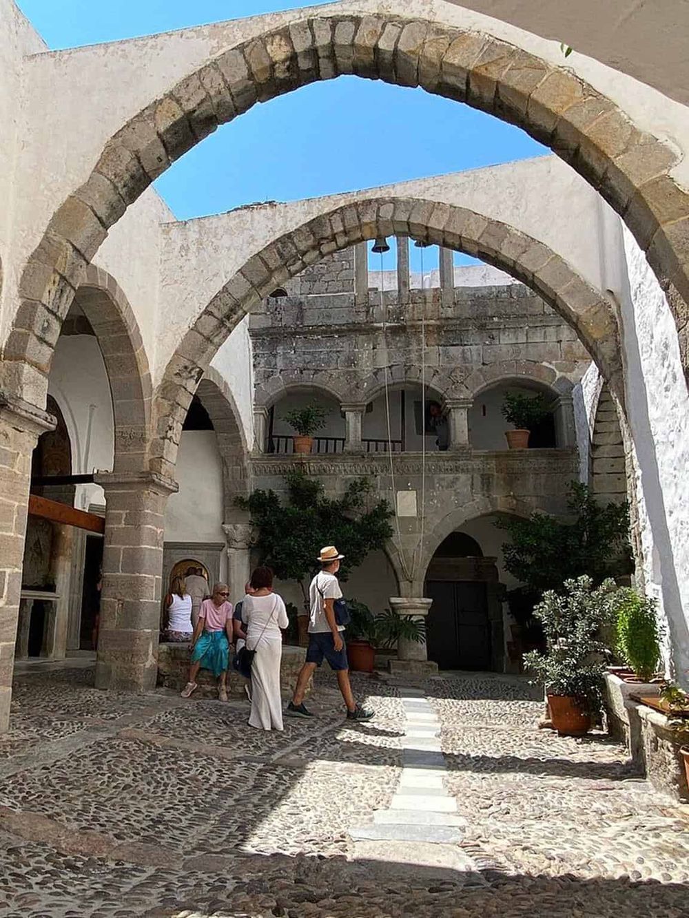 Archaeological courtyard with stone arches, historic architecture, and tourists exploring the site.