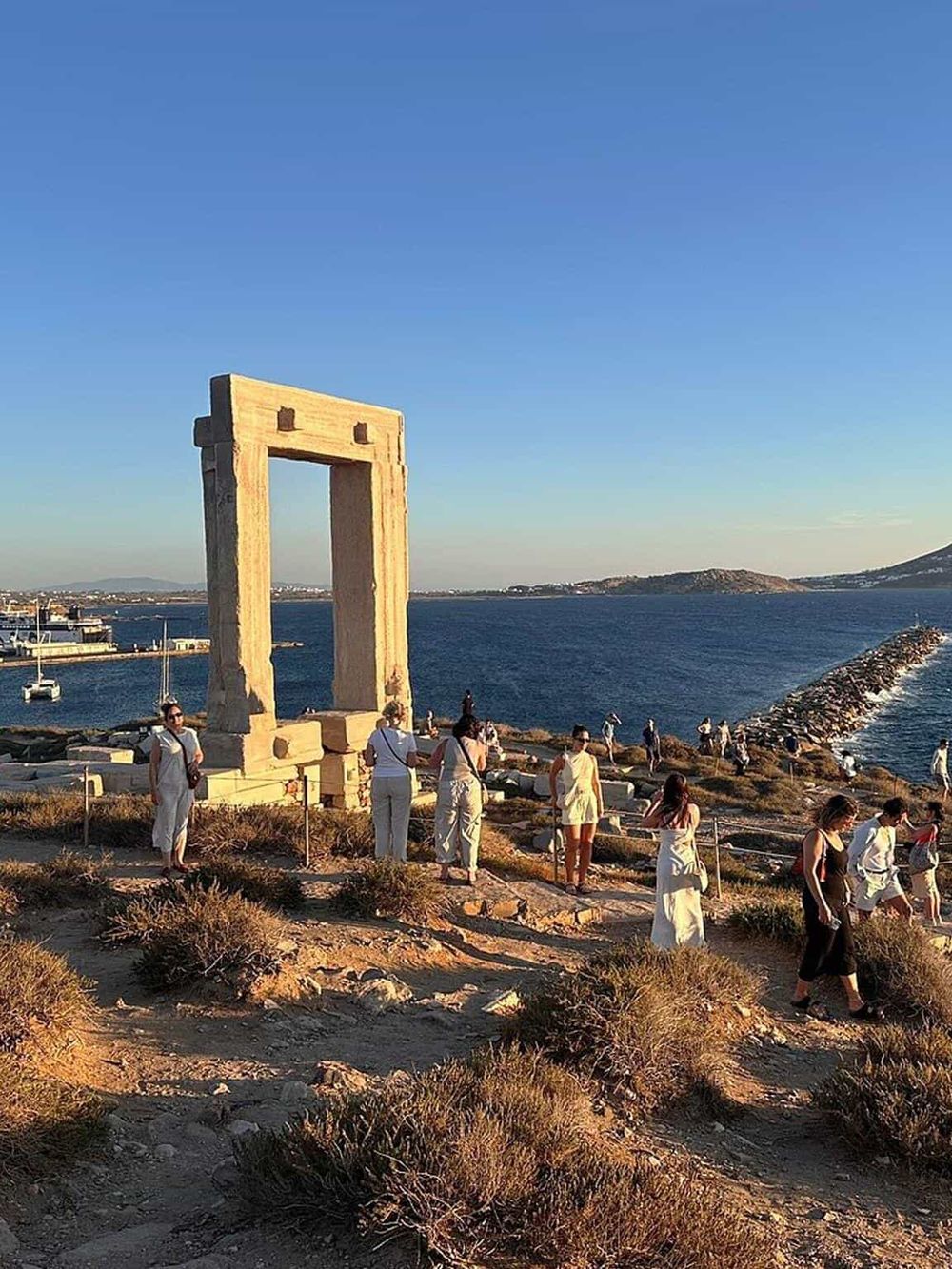 Ancient Greek Temple of Apollo at Portara, Naxos island, Greece, sunset view with visitors exploring the historic site.