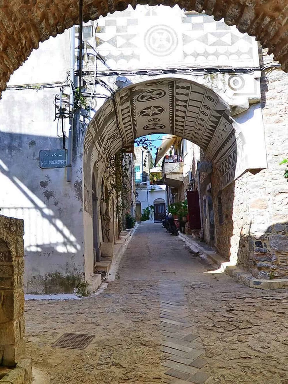 Charming alleyway with historic arch, traditional architecture, and cobblestone street in a Mediterranean town.