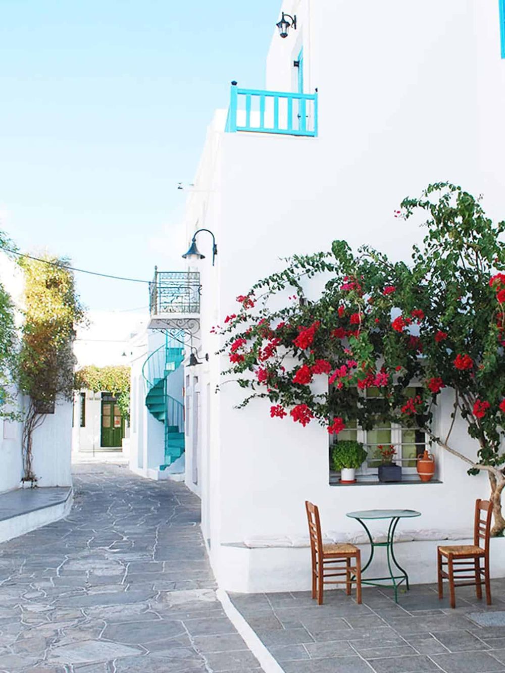 Colorful Greek island street with whitewashed buildings, vibrant flowers, and a charming outdoor seating area.