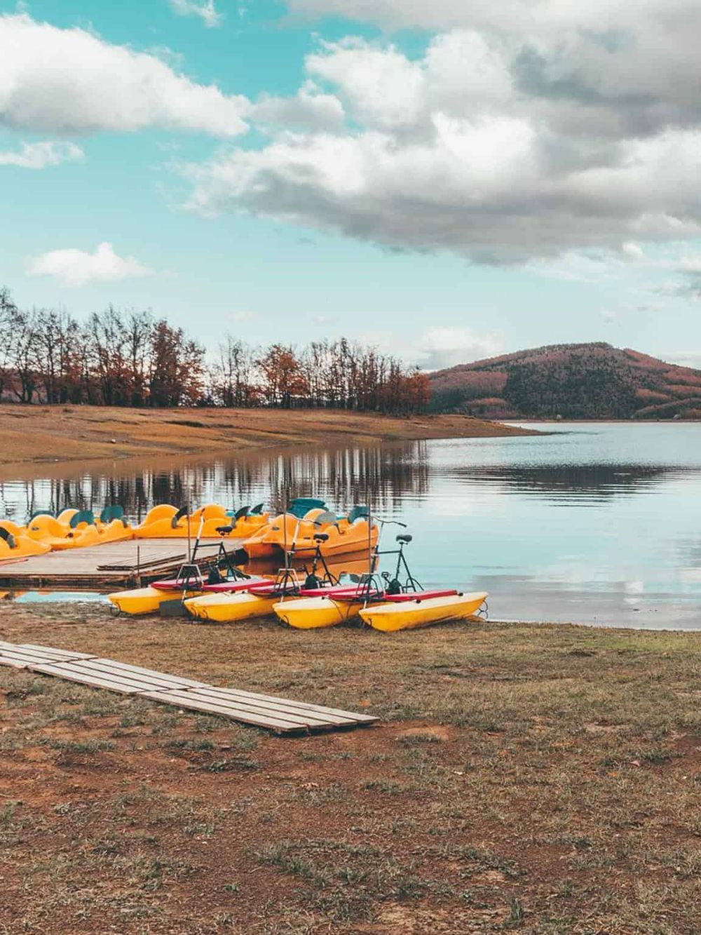 Colorful pedal boats on a lake with autumn trees and mountains in the background.