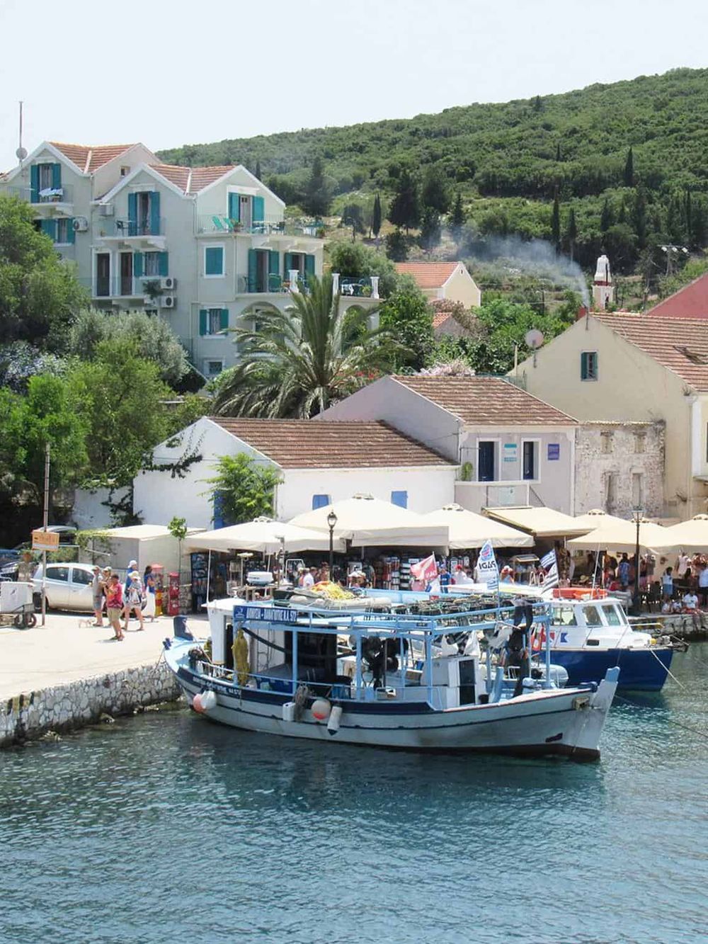 Charming coastal village with boats, seaside cafes, and green hillside scenery, perfect for exploring with QuestForDirections.