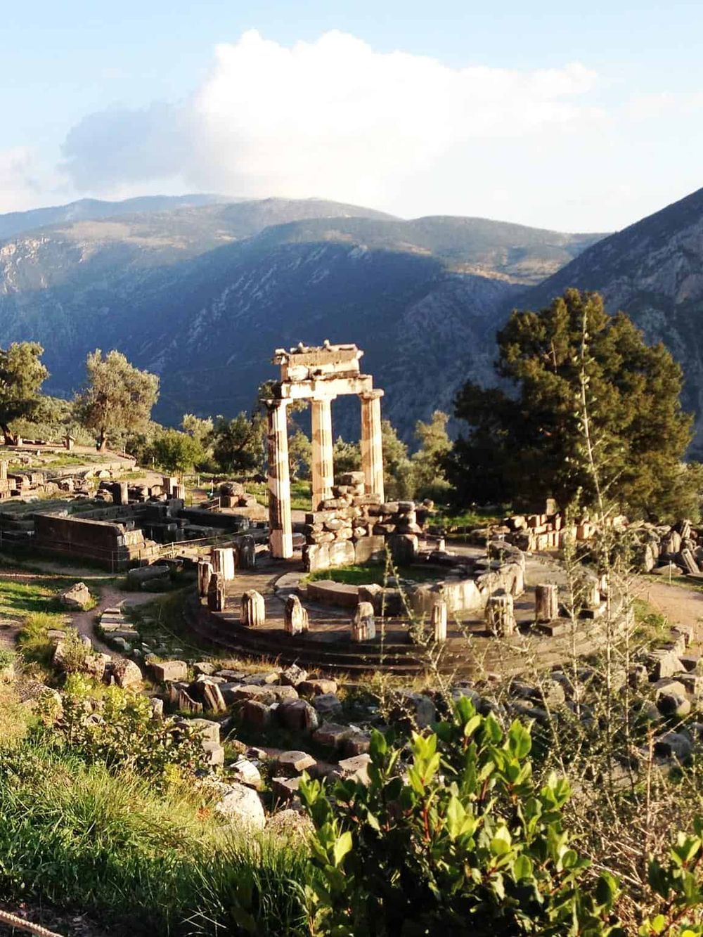 Ancient Greek ruins in a scenic mountain landscape with lush greenery and blue skies.