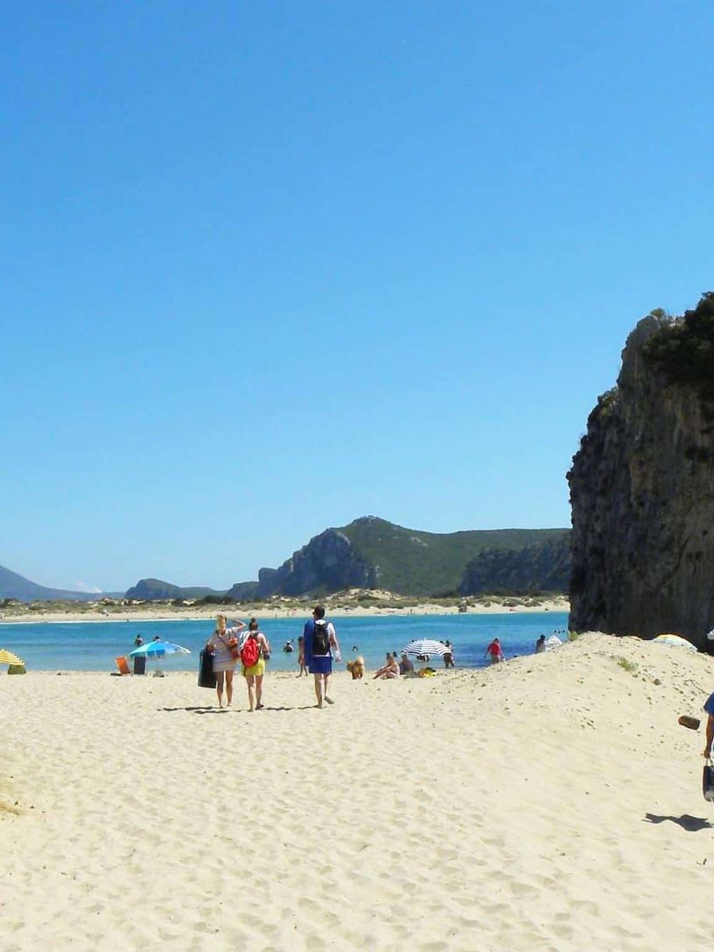 Bright sunny beach with travelers enjoying sandy shores, turquoise waters, and scenic cliffs in the background.