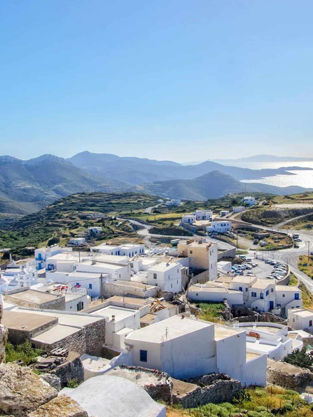 Charming white village with blue accents on hillside overlooking scenic mountains and sea, Greece destination.
