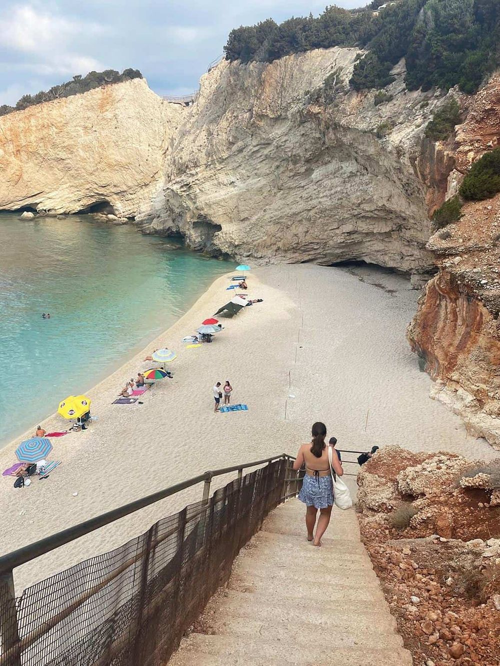 Secluded coastal cove with sandy beach, colorful umbrellas, and towering cliffs, perfect for vacation and relaxation.