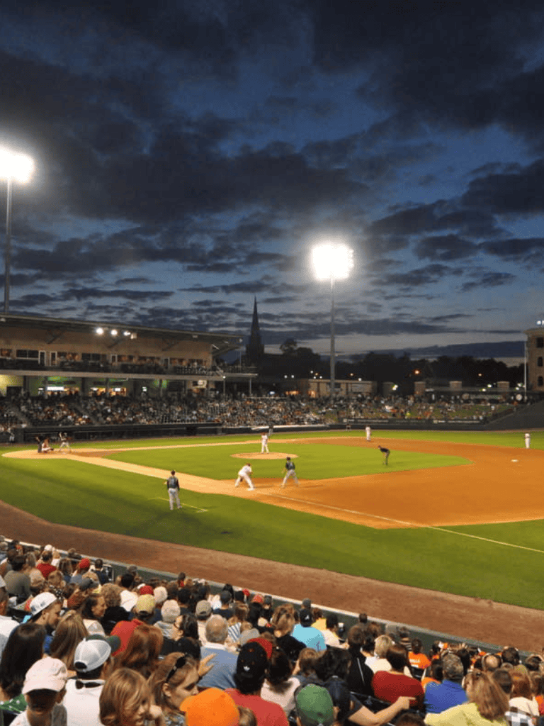 Night baseball game at a stadium with bright lights and cheering crowd, lively sports atmosphere.