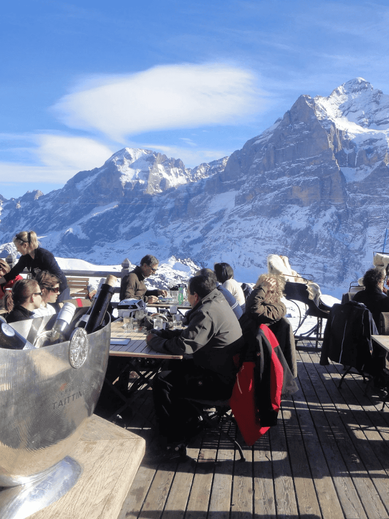 Snow-capped mountain dining terrace with people enjoying scenic views, beautiful winter landscape, outdoor mountain restaurant.